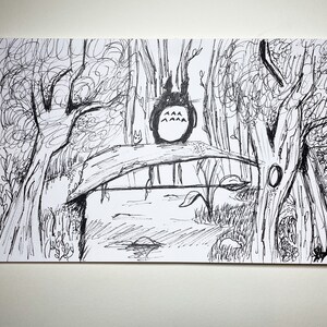 May include: Black and white ink drawing depicting a forest scene with a bridge over water. A large, round, cartoon creature with pointed ears sits on the bridge. Trees and foliage surround the bridge, creating a whimsical landscape.