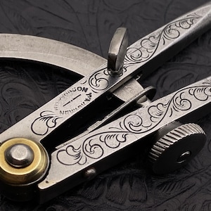 May include: A silver compass with intricate floral engravings. The compass is marked "NEWARK N.J. JOHNSON".