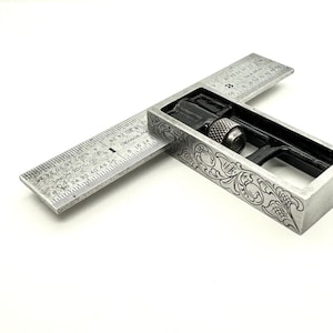 May include: A silver metal try square with a ruler marked in inches and fractions of an inch. The ruler is labeled "UNION TOOL CO. ORANGE MASS". The try square has a decorative floral design etched into the metal.