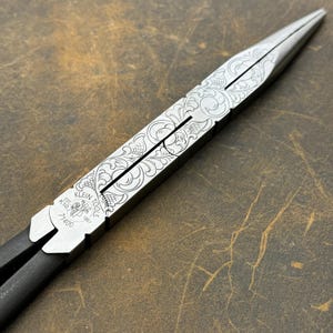 May include: A pair of silver-colored pliers with a black handle. The pliers are engraved with a floral design and the text "Klein Tools Est. 1857 K10 71400".