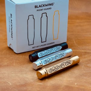 May include: A set of three Blackwing Point Guards in black, silver, and gold, each with an engraved floral design. The box in the background reads "BLACKWING POINT GUARD" and "SET OF 3 POINT GUARDS".