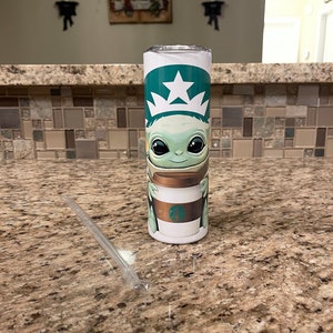 Puede incluir: Un vaso de acero inoxidable con el logotipo verde y blanco de Starbucks y una imagen de dibujos animados de Grogu de The Mandalorian. El vaso tambi&eacute;n tiene una pajita de pl&aacute;stico transparente.