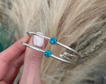 May include: Two silver bangle bracelets with turquoise stones. The bracelets are stacked on top of each other and have the word "Sterling" engraved on them.