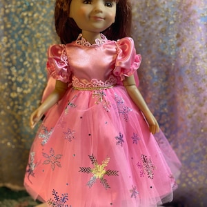 May include: A pink doll wearing a pink dress with a gold trim and snowflake pattern. The doll has brown hair and is wearing a flower crown.