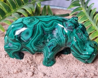 May include: A green malachite hippopotamus figurine. The hippo is carved from a single piece of malachite, and the intricate swirling patterns of the stone are visible throughout the figurine.