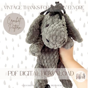 Könnte beinhalten: Häkelanleitung für ein graues Eeyore Plüschtier. Das Muster ist als digitaler PDF-Download erhältlich. Das Bild zeigt das fertige Plüschtier, das von einer Hand gehalten wird.