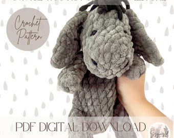 May include: Crochet pattern for a gray Eeyore plush toy. The pattern is available as a digital PDF download. The image shows the finished plush toy being held by a hand.