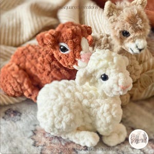 May include: Three crocheted stuffed animals: a brown alpaca, a white lamb, and a brown and white guinea pig. The animals are sitting on a striped blanket.