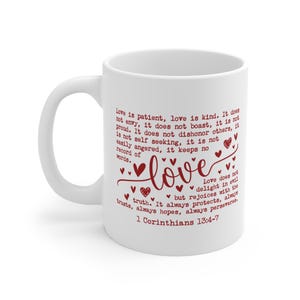 Könnte beinhalten: Weißer Keramikbecher mit gebogenem Henkel. Der Becher zeigt das Wort "love" in Schreibschrift, umgeben von Herzen, und ein Zitat aus 1. Korinther 13:4-7 in burgunderrotem Text.