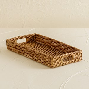 May include: A rectangular woven tray with two handles. The tray is made of natural rattan and has a light brown color.