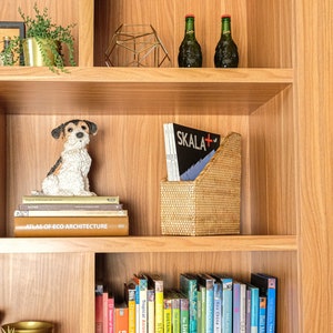 May include: A wooden bookshelf with a variety of items, including books, a dog figurine, a magazine holder, and two glass bottles. The bookshelf is made of light wood and has a warm, inviting feel.