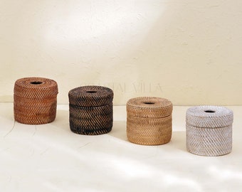 May include: Four woven wicker tissue box covers in different colors and patterns. The covers are round and have a lid. The covers are arranged in a row from left to right. The covers are on a white surface.