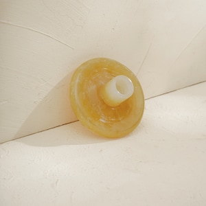 May include: A yellow, round, ceramic candle holder with a small, white, cylindrical opening in the center.