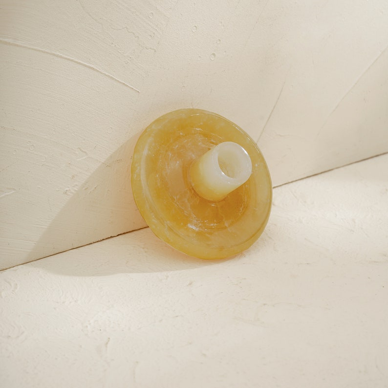May include: A yellow, round, ceramic candle holder with a small, white, cylindrical opening in the center.