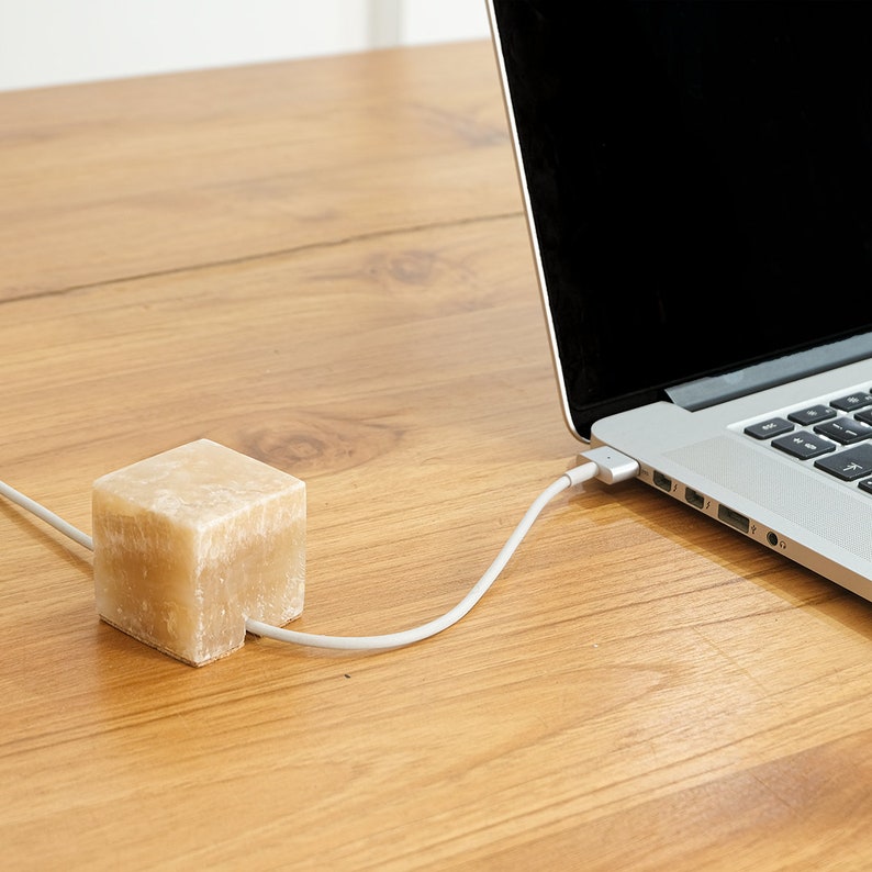 May include: A beige stone cable organizer on a wooden table with a laptop connected to it.