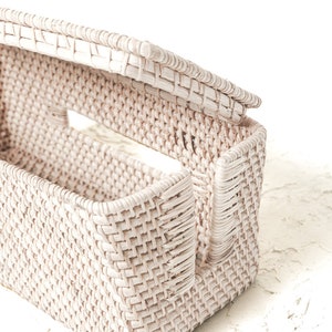 May include: A white wicker basket with a lid, the lid is open and the basket is empty. The basket is woven with a tight pattern and has a rectangular shape.