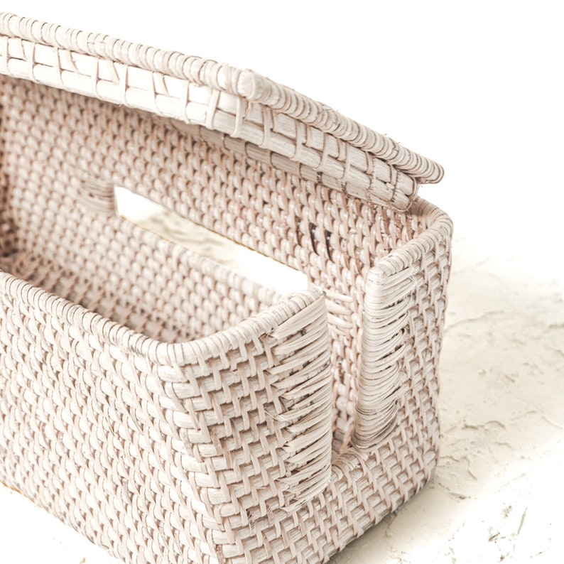 May include: A white wicker basket with a lid, the lid is open and the basket is empty. The basket is woven with a tight pattern and has a rectangular shape.