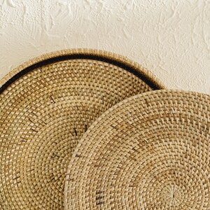 May include: Two round woven wicker trays, one stacked on top of the other. The trays are made of natural brown wicker and have a circular shape.