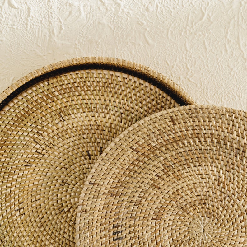 May include: Two round woven wicker trays, one stacked on top of the other. The trays are made of natural brown wicker and have a circular shape.