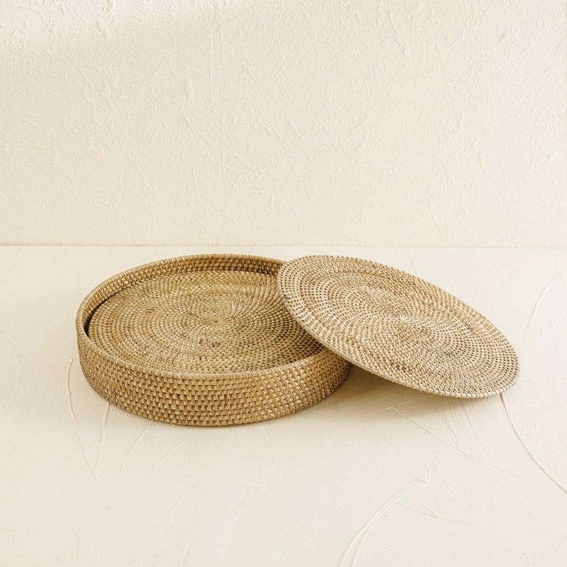 May include: A round woven tray with a lid, both made of natural rattan. The tray is open and the lid is sitting next to it.