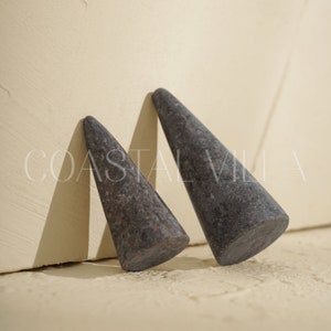May include: Two gray stone cone-shaped objects. The cones are smooth and have a slightly textured surface.
