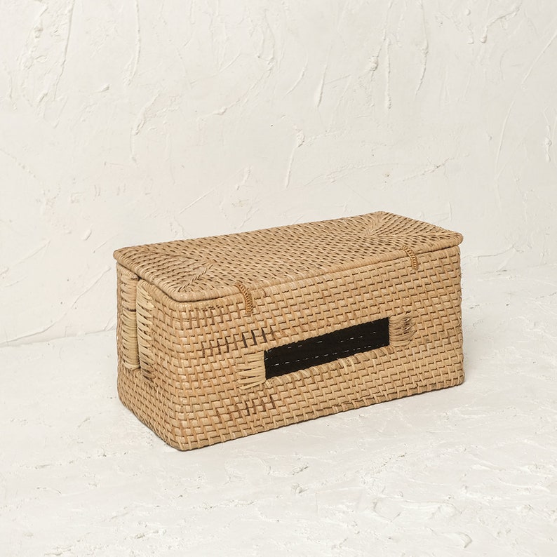 May include: A woven wicker storage box with a rectangular shape and a black opening on the front. The box is made of natural materials and has a light brown colour.