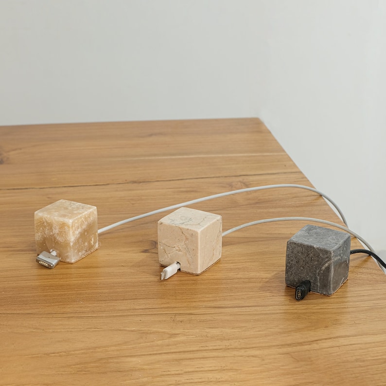 May include: Three white and gray marble cable organizers with white cords plugged into each. The organizers are on a light brown wooden surface.