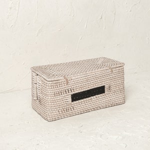 May include: White wicker storage box with a rectangular shape and a black opening on the front. The box is woven with a fine, intricate pattern.