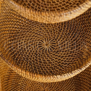 May include: A set of three woven wicker baskets with a circular shape and a natural brown colour. The baskets are stacked on top of each other, with the top basket slightly out of focus.