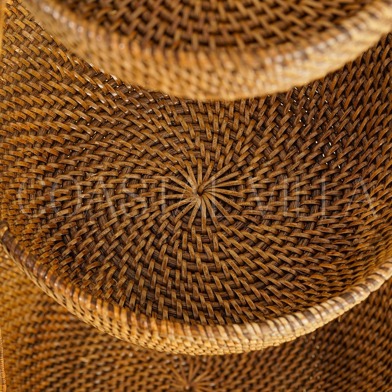 May include: A set of three woven wicker baskets with a circular shape and a natural brown colour. The baskets are stacked on top of each other, with the top basket slightly out of focus.