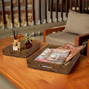 May include: Two woven wicker trays, one with a glass bottle of diffuser sticks and a small potted plant, the other with magazines titled "Living" and "Interiors in Red".