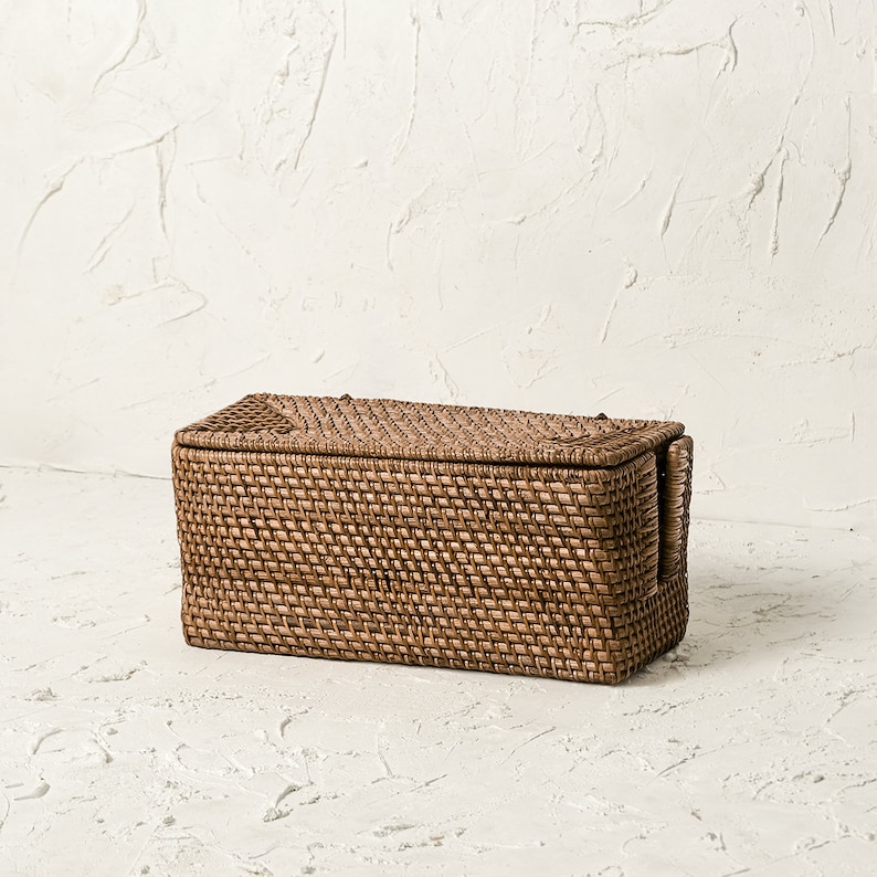 May include: A rectangular woven storage basket with a lid and handles. The basket is made of natural brown wicker and has a woven pattern.