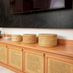 Peut inclure: Trois paniers ronds en osier de couleur naturelle posés sur une étagère en bois avec des portes de placard en rotin tissé.