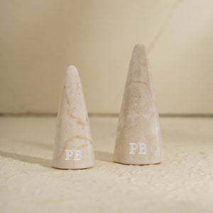 May include: Two white marble cone-shaped ring holders with the initials "PB" engraved on the bottom.