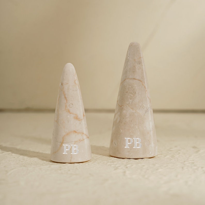 May include: Two white marble cone-shaped ring holders with the initials "PB" engraved on the bottom.