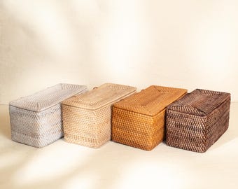 May include: Four rectangular woven storage boxes with lids, arranged in a row. The boxes feature a tight, uniform weave pattern and are presented in a gradient of colors, ranging from light grey to beige, golden tan, and dark brown.