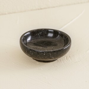 K&ouml;nnte beinhalten: Eine kleine, runde schwarze Marmorschale mit einer glatten, polierten Oberfl&auml;che. Die Schale ist perfekt f&uuml;r Schmuck, Schl&uuml;ssel oder andere kleine Gegenst&auml;nde.
