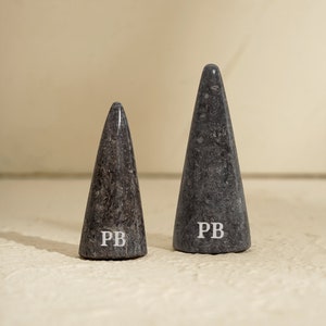 May include: Two gray marble cone-shaped ring holders with the letters "PB" engraved on the bottom.