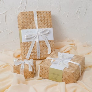 May include: Three woven baskets with white ribbon and a tag that says "This package is for you". The baskets are on a light beige fabric.
