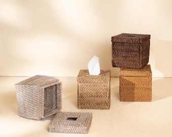 Könnte beinhalten: Eine Sammlung quadratischer Taschentuchboxen aus geflochtenem Rattan in verschiedenen Braun- und Grautönen. Jede Box verfügt über einen abnehmbaren Deckel mit einer zentralen rechteckigen Öffnung, wobei eine Box offen dargestellt ist.