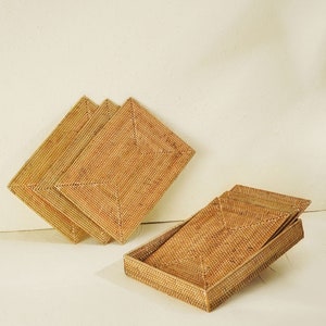 Pode incluir: Conjunto de quatro tapetes de vime tecido em cor bege natural. Os tapetes estão empilhados uns sobre os outros, com um tapete dobrado ao meio para criar uma bandeja.