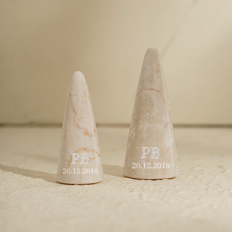 May include: Two small, cone-shaped marble ring holders with the initials "PB" and the date "20.12.2018" engraved on them.