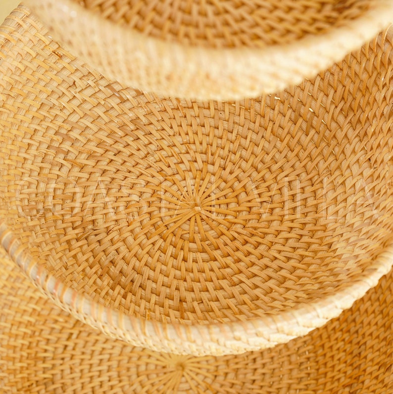 May include: A set of three woven baskets made from natural materials. The baskets are stacked on top of each other, with the largest basket at the bottom and the smallest basket at the top. The baskets are a light brown colour and have a circular shape.