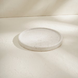 May include: A white marble tray with a smooth, round surface. The tray is ideal for displaying small items or serving snacks.