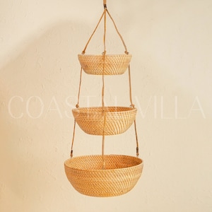 May include: Three hanging wicker baskets with a natural woven texture. The baskets are suspended from a ceiling or wall by brown cords.