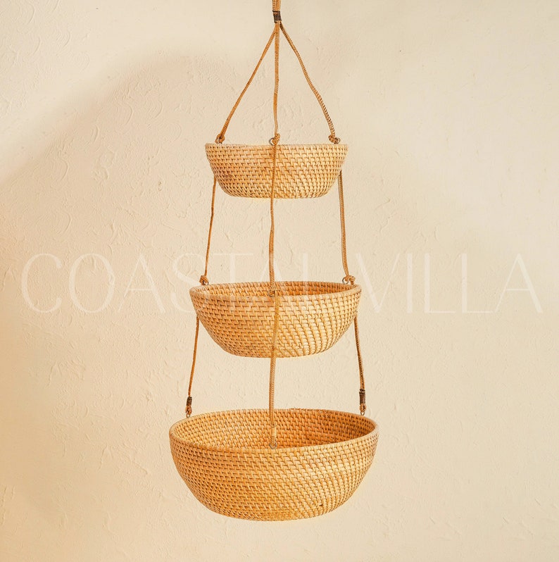 May include: Three hanging wicker baskets with a natural woven texture. The baskets are suspended from a ceiling or wall by brown cords.