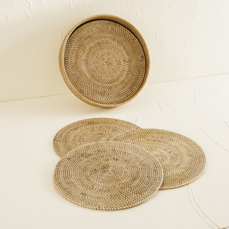May include: Set of four round woven rattan placemats and a matching larger woven rattan tray. The placemats and tray are a light brown color.