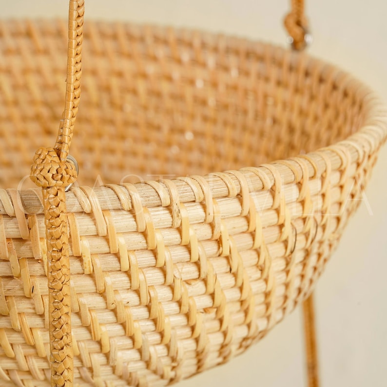 May include: A natural woven hanging basket with a light brown colour and a woven pattern. The basket has a round shape and is made of natural materials.