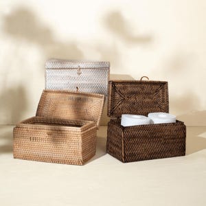 Könnte beinhalten: Drei rechteckige Aufbewahrungsboxen aus geflochtenem Rattan mit Klappdeckeln. Eine Box ist hellbeige, eine dunkelbraun und eine weiß. Die dunkelbraune Box ist geöffnet und enthält zwei weiße Toilettenpapierrollen, während die beige Box offen ist.