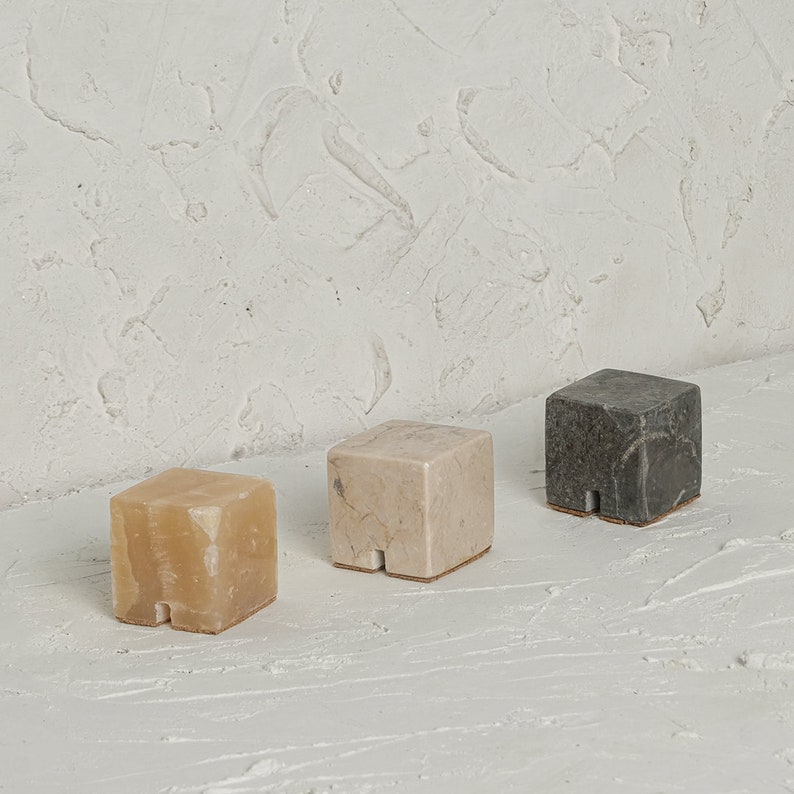 May include: Three small, square, decorative blocks made of different types of marble. The blocks are beige, light brown, and gray. The blocks are arranged in a row on a white surface.